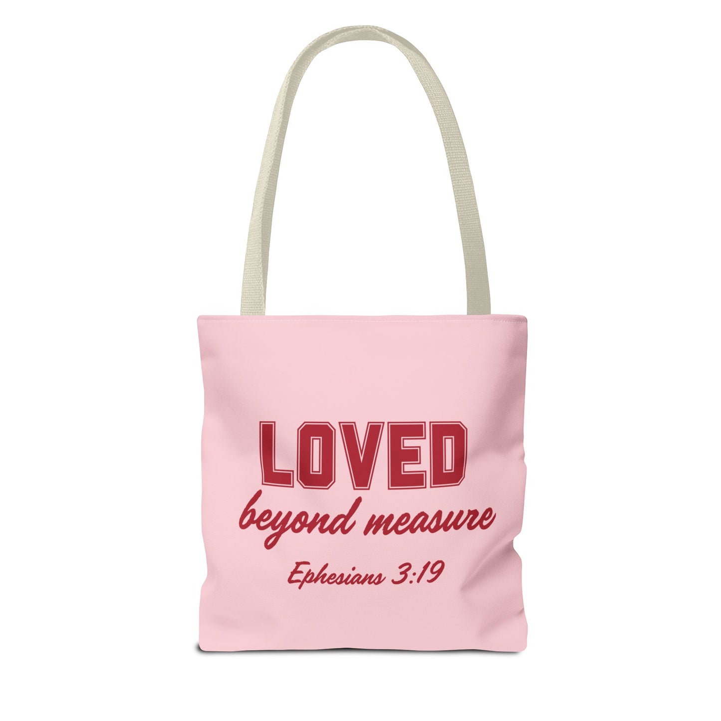 A pink canvas tote bag with long handles, featuring the phrase "LOVED beyond measure" in bold red letters, followed by the Bible verse reference "Ephesians 3:19" in smaller red font.