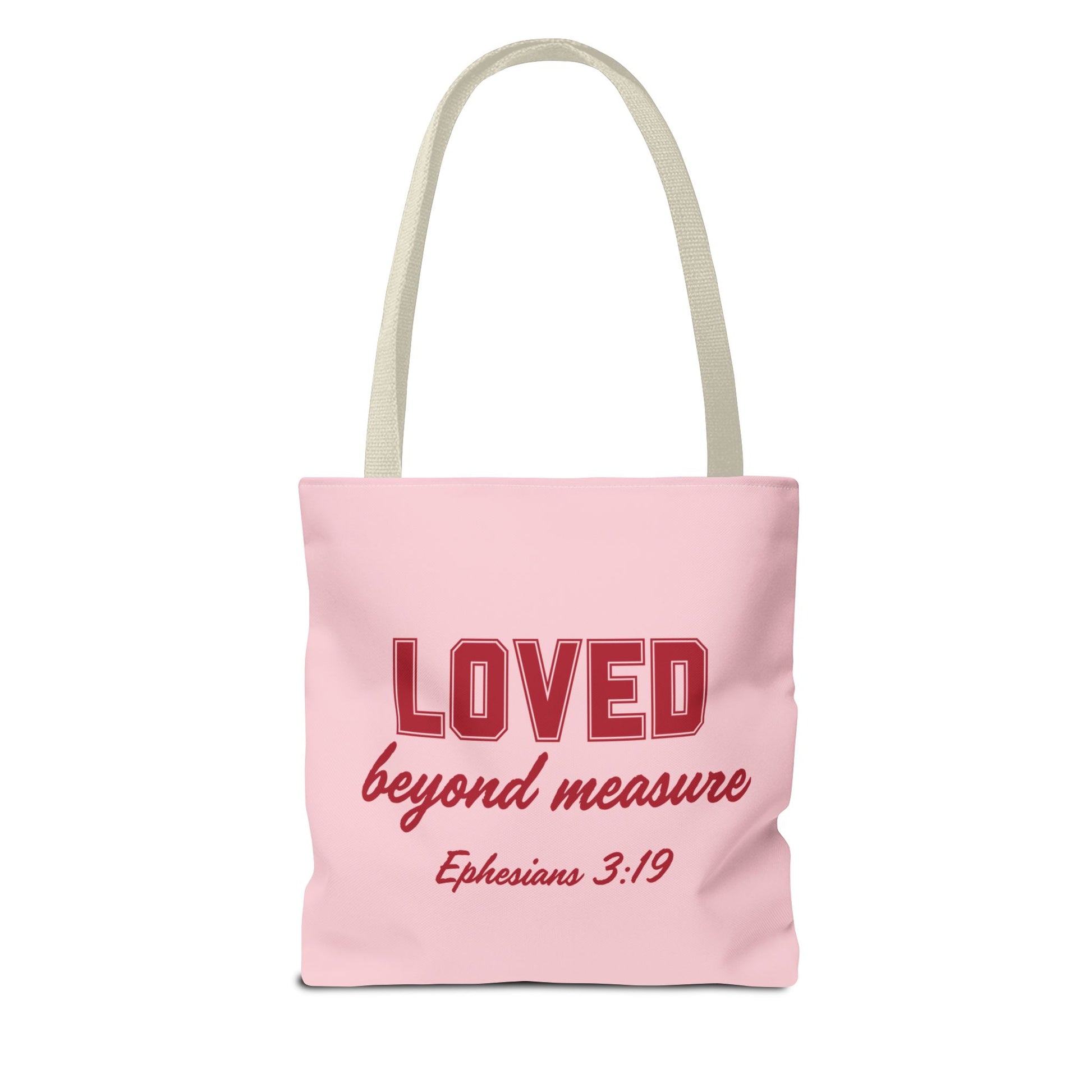 A pink canvas tote bag with long handles, featuring the phrase "LOVED beyond measure" in bold red letters, followed by the Bible verse reference "Ephesians 3:19" in smaller red font.