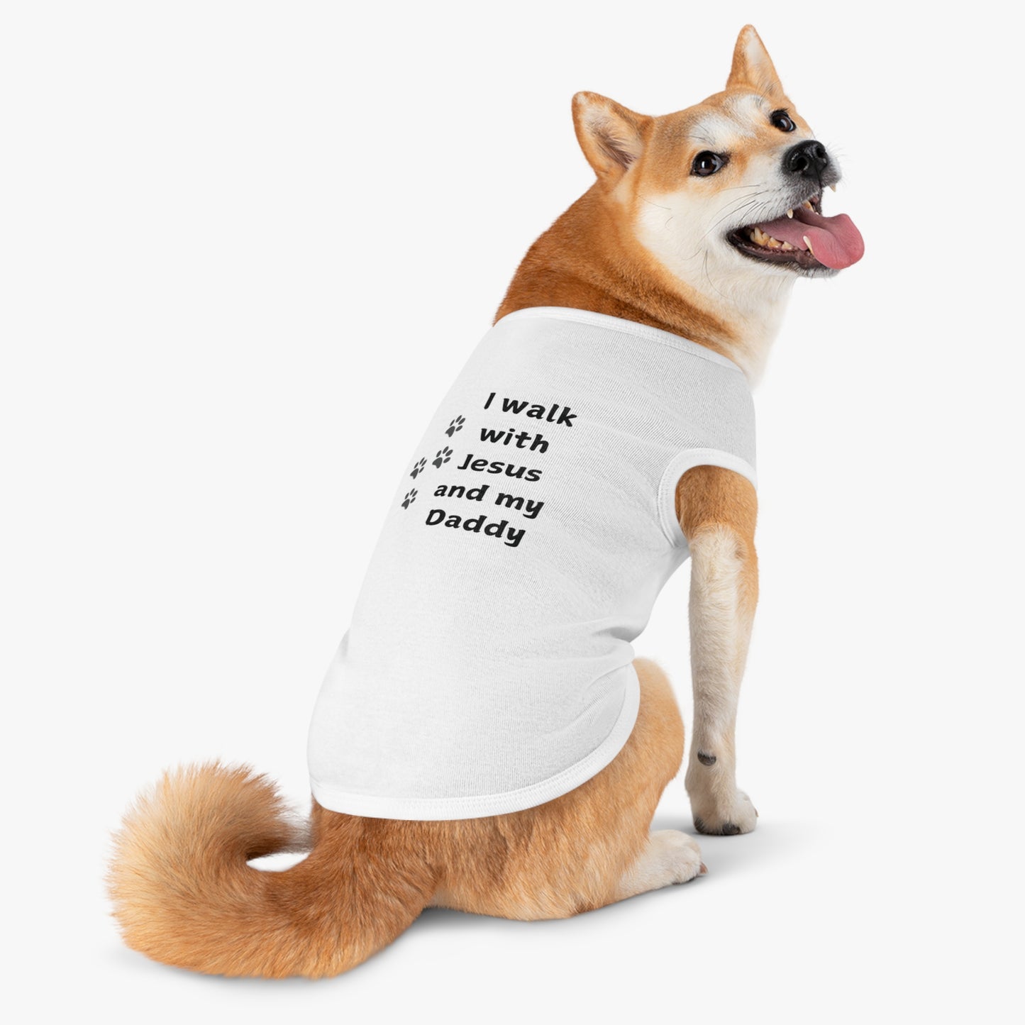 A Shiba Inu dog wearing a white t-shirt with the text "I walk with Jesus and my Daddy" printed in black, along with three paw prints.