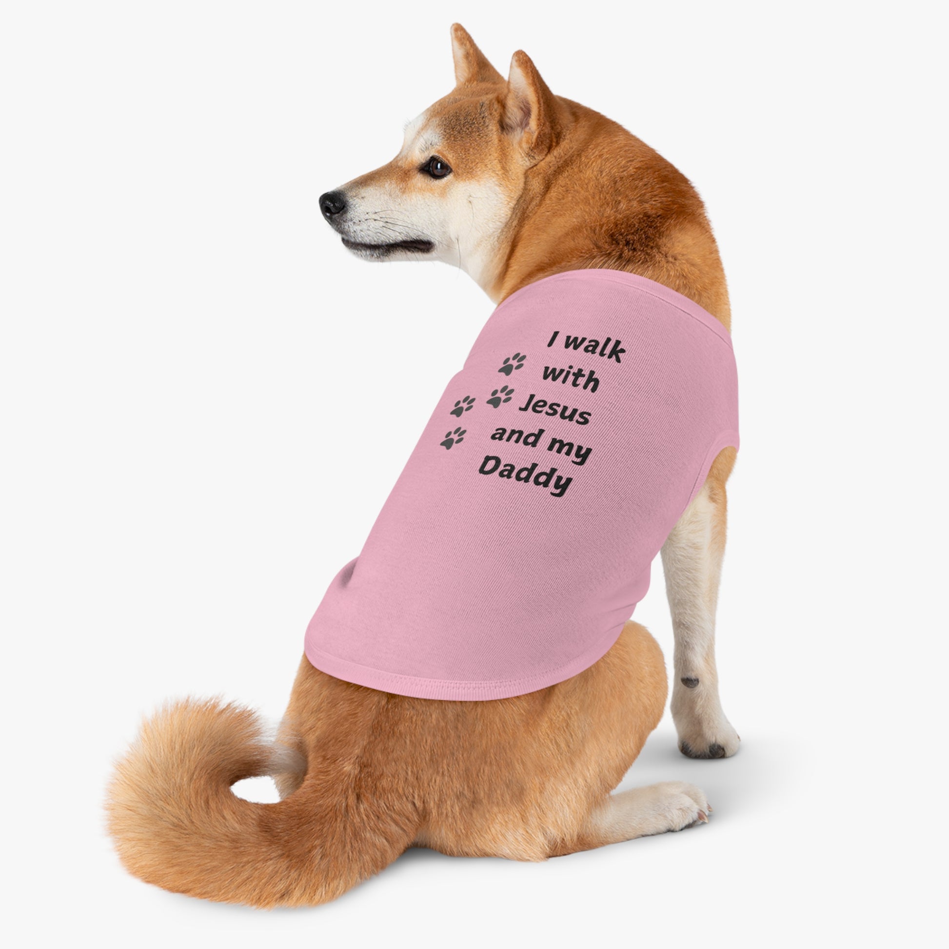 Shiba Inu dog wearing a pink shirt. The shirt features the text "I walk with Jesus and my Daddy" along with paw print graphics.