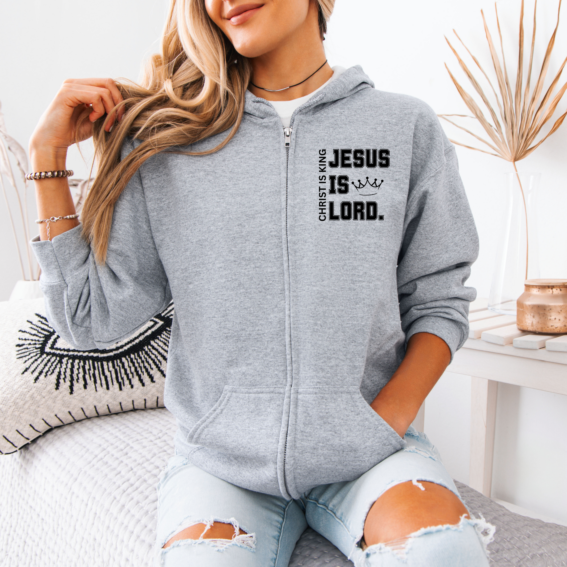 A woman wearing a gray zip-up hoodie with the words "JESUS IS LORD" and "CHRIST IS KING" printed on it