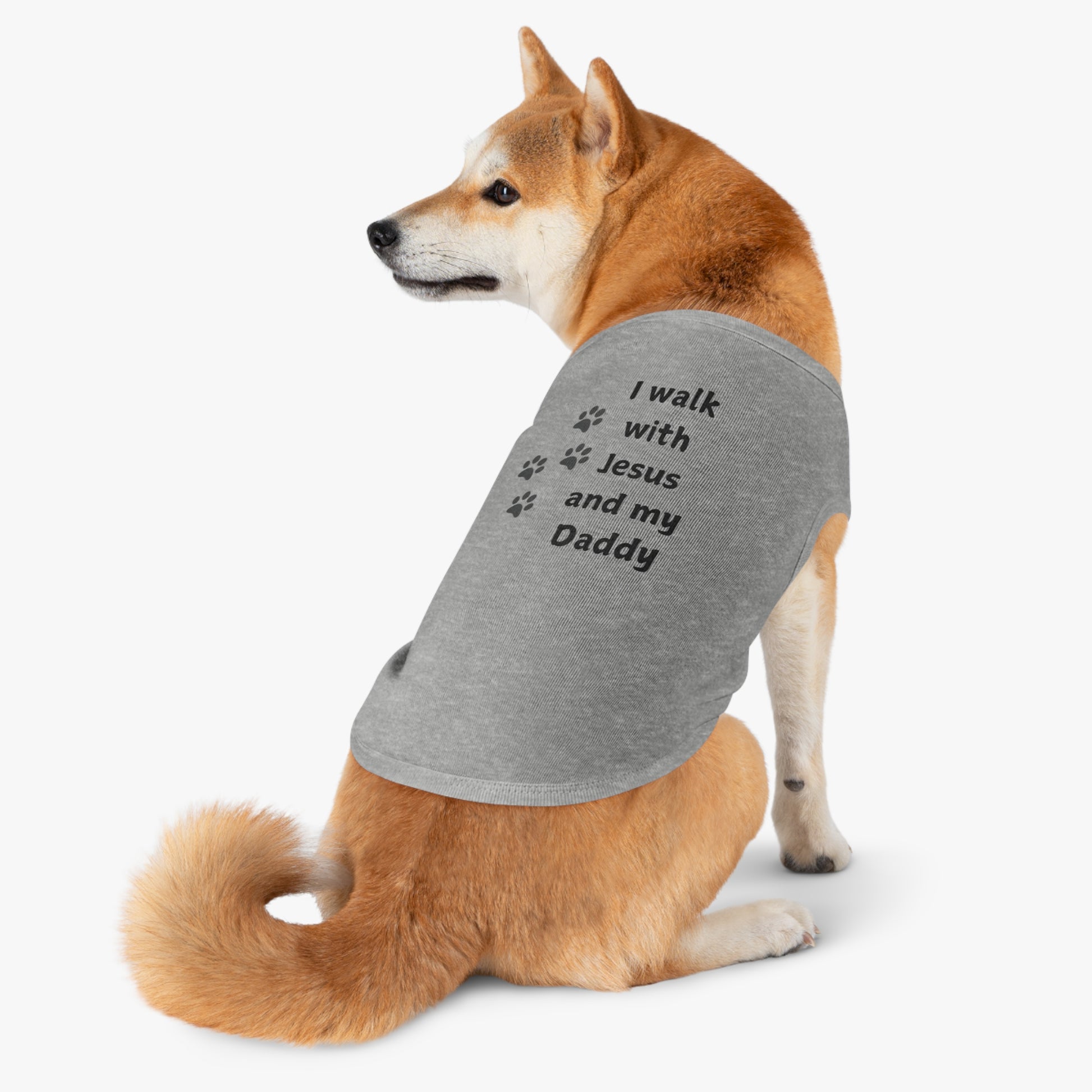 Shiba Inu dog wearing a grey shirt with the black text "I walk with Jesus and my daddy