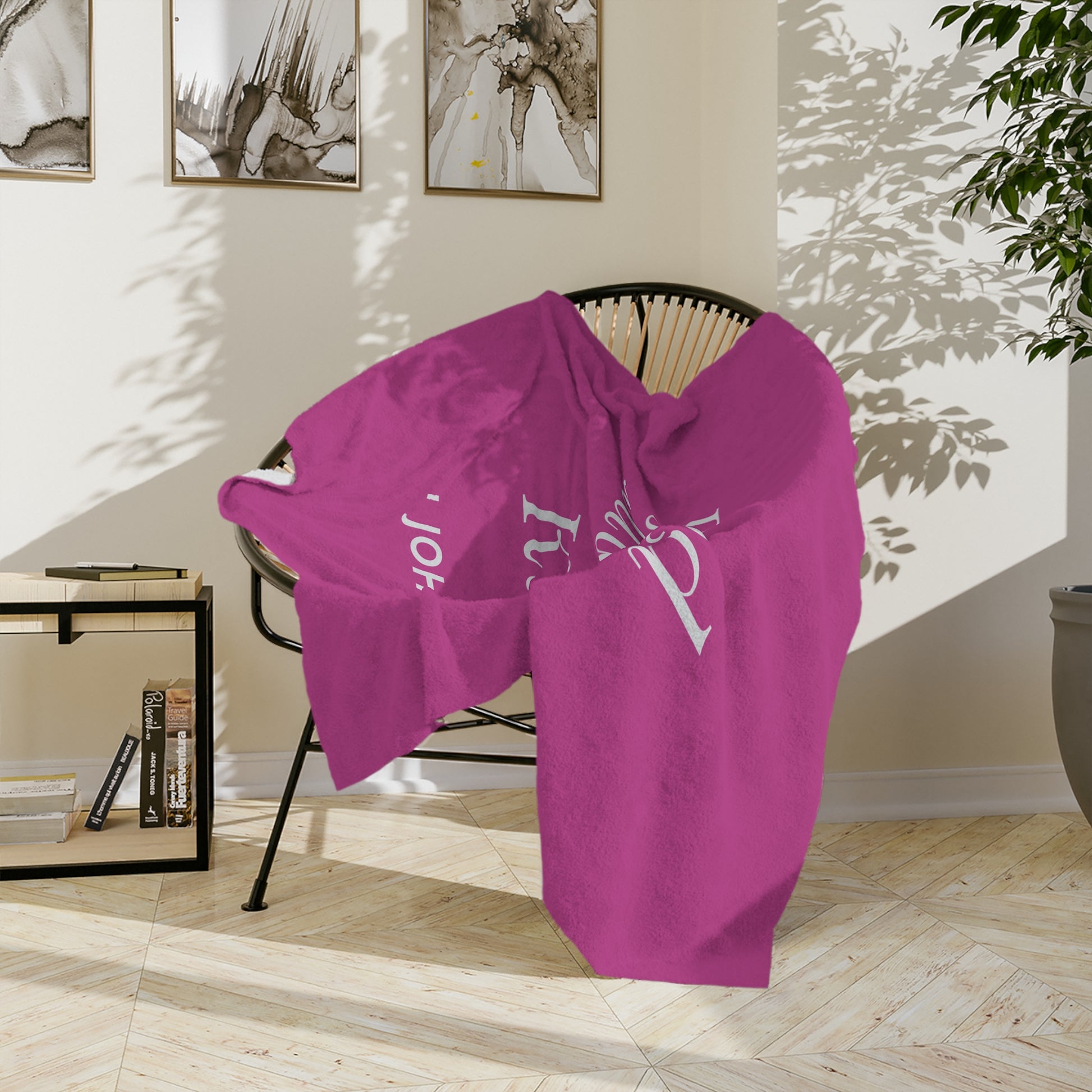 A pink throw blanket with the word "Family" and the name "John" printed on it. The blanket is draped over a chair in a bright living room